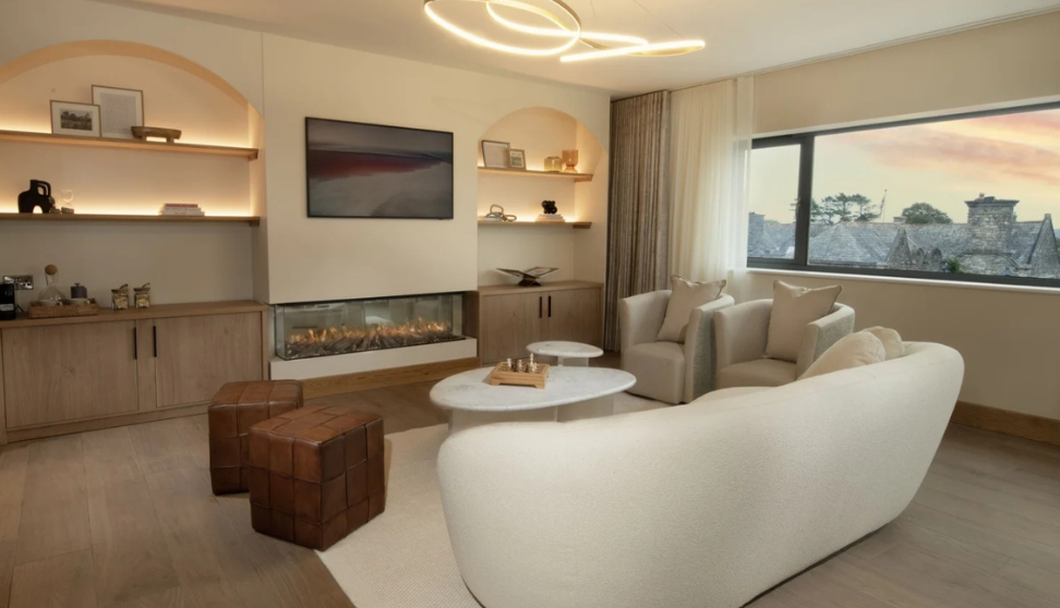 A hotel room with white sofas, tv and a fireplace.